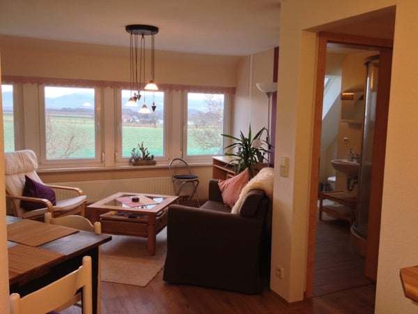 Wohnraum mit Sofa, Panoramafenstern und Blick durch die Tür ins Bad
