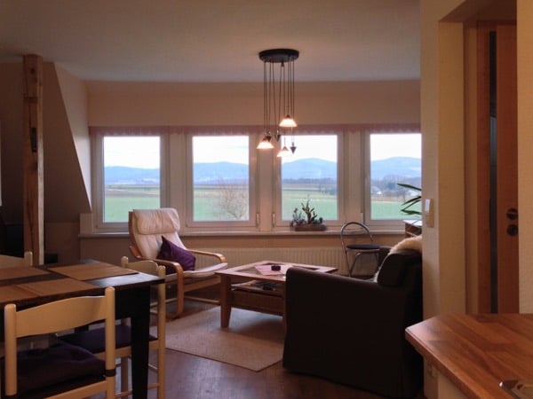 Wohnraum mit vier Panoramafenstern und Blick über Felder ins Gebirge