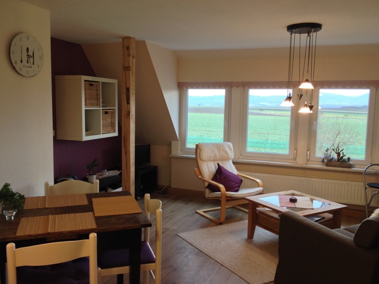 Heller Wohnraum der Ferienwohnung mit Essplatz, Panoramafenstern und Blick über Felder auf das Zittauer Gebirge